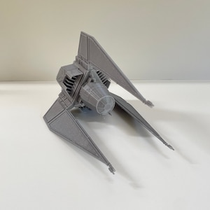 May include: A gray 3D printed model of a TIE Interceptor starfighter from the Star Wars universe. The model is detailed and features the iconic triangular wings and engine.