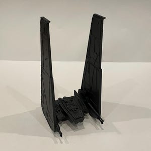 Puede incluir: Un modelo de nave espacial TIE Interceptor negro. El modelo está hecho de plástico y tiene un diseño detallado. La nave tiene dos alas grandes y una pequeña cabina.