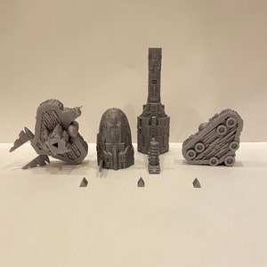 May include: A set of five 3D printed grey spaceship models. The models are detailed and intricate, with various shapes and textures. The models are arranged on a white surface.