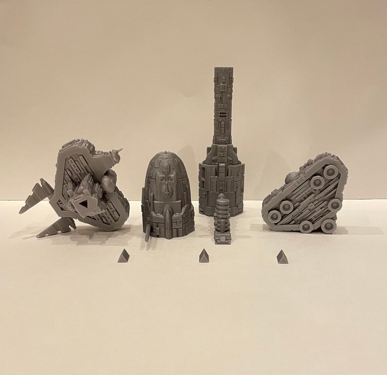 May include: A set of five 3D printed grey spaceship models. The models are detailed and intricate, with various shapes and textures. The models are arranged on a white surface.
