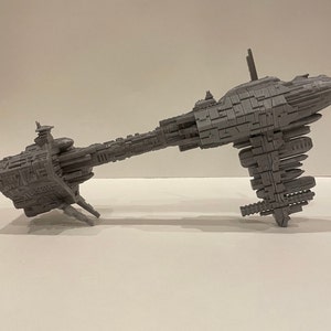 May include: A grey, detailed model of a spaceship with a long, thin body and a large, round cockpit. The model is made of plastic and has a textured surface.