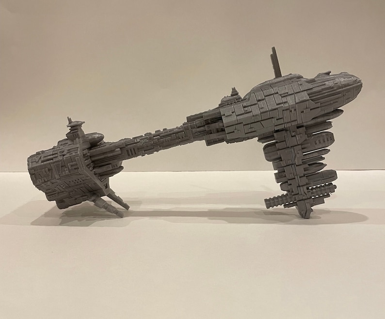 May include: A grey, detailed model of a spaceship with a long, thin body and a large, round cockpit. The model is made of plastic and has a textured surface.