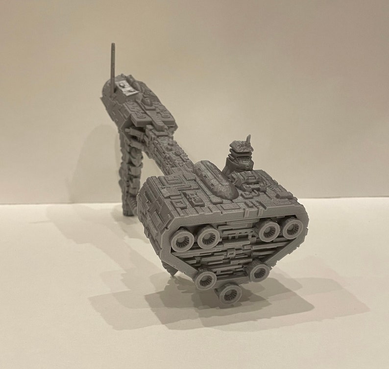 May include: A grey 3D printed model of a spaceship with a long, thin body and a large, round engine section at the rear. The spaceship has a small, rectangular cockpit at the front and a series of small, round windows along the side.