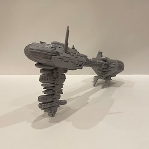 May include: A grey 3D printed model of a spaceship with a long, thin body and a large, round cockpit. The spaceship has a series of small, rectangular windows along the side of the body.