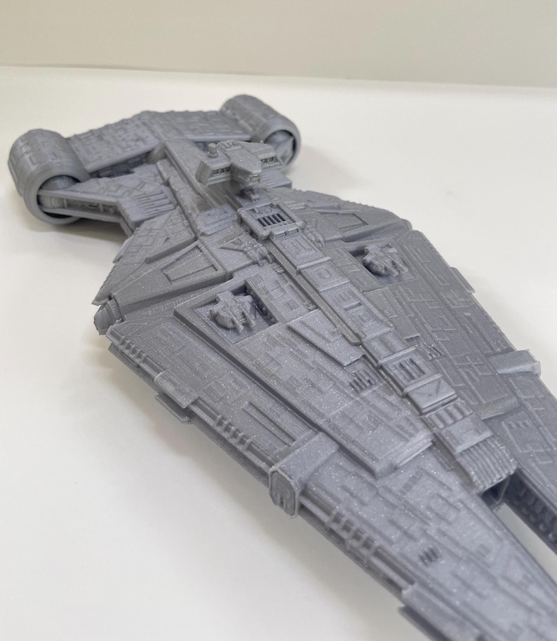 Op de afbeelding: Een gedetailleerd, grijs model van een ruimteschip met ingewikkelde panelen en motordetails. Het model heeft een textuuroppervlak en een symmetrisch ontwerp, wat wijst op een sciencefictionthema. Het ontwerp van het schip omvat meerdere rechthoekige en cilindrische componenten.