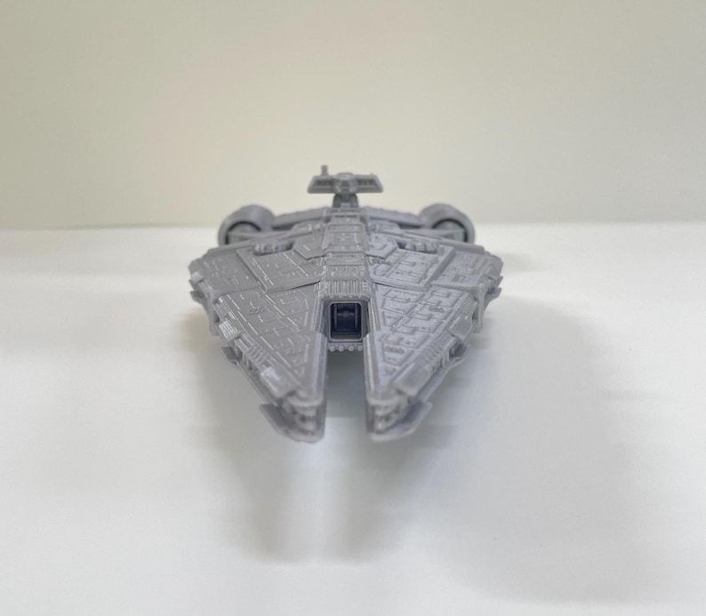 Op de afbeelding: Een grijs model ruimteschip met ingewikkelde details, met een centraal lichaam en vleugelachtige structuren. Het speelgoed ruimteschip is ontworpen met een symmetrische lay-out en lijkt van plastic te zijn. Het model staat tegen een effen witte achtergrond.