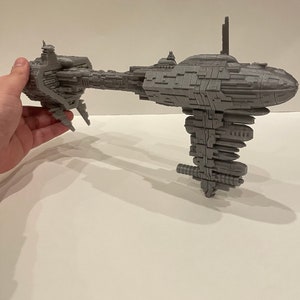 May include: A grey 3D printed model of a spaceship with a long, thin body and a large, round engine section. The model is detailed with many small parts and features.