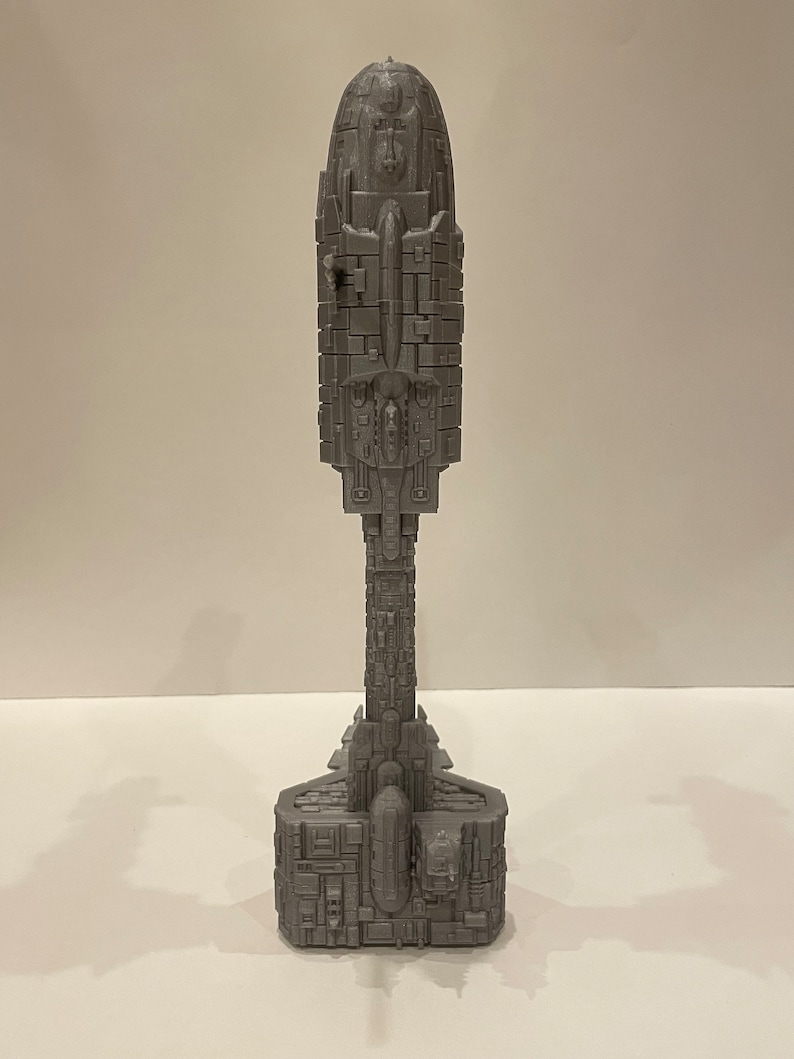 May include: A grey 3D printed model of a spaceship with a long, cylindrical body and a rounded top. The model has a detailed design with many small, intricate features.