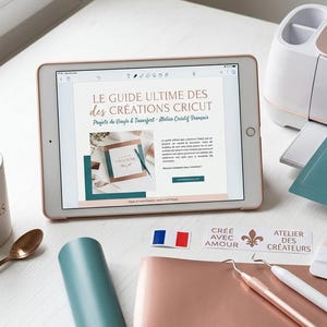 Peut inclure: Un espace de travail avec une machine Cricut Maker 3, une tablette affichant un guide Cricut et des fournitures de création. Comprend une tasse à café, des tapis de découpe, des rouleaux de vinyle et des outils. Le texte sur la tablette est "LE GUIDE ULTIME DES CRÉATIONS CRICUT".