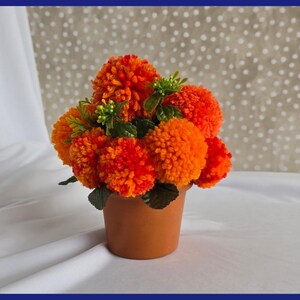 May include: A terracotta pot filled with a bouquet of orange and yellow pom-pom flowers.