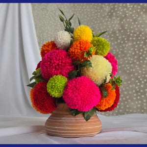 May include: A vibrant bouquet of colorful pom-pom flowers in a terracotta vase. The arrangement features bright pink, red, orange, yellow, green, and white pom-poms, creating a cheerful and eye-catching display. The vase has horizontal stripes.