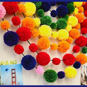 May include: A rainbow garland made of colorful yarn pom-poms. The garland is strung together with black thread and features a variety of colors, including red, orange, yellow, green, blue, and purple.