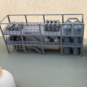 May include: A miniature industrial model featuring a multi-level structure with cylindrical tanks, storage racks, and various processing units. The model is primarily gray, with detailed components and a realistic design, suggesting a factory or plant.