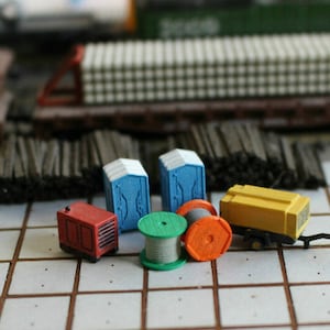 May include: A collection of miniature model building supplies, including two blue portable toilets, a red generator, a yellow construction vehicle, and two spools of wire, one green and one orange.