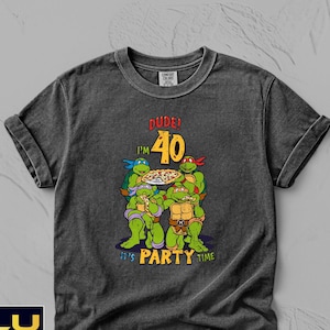 May include: Dark gray t-shirt featuring a graphic of the Teenage Mutant Ninja Turtles holding a pizza, with the text "DUDE! I'M 40. IT'S PARTY TIME." The shirt has a crew neck and short sleeves.