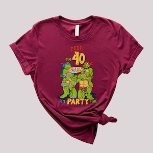 May include: A maroon t-shirt with a graphic of four Teenage Mutant Ninja Turtles holding pizza slices. The text "DUDE! I'M 40 IT'S PARTY TIME" is printed on the shirt.