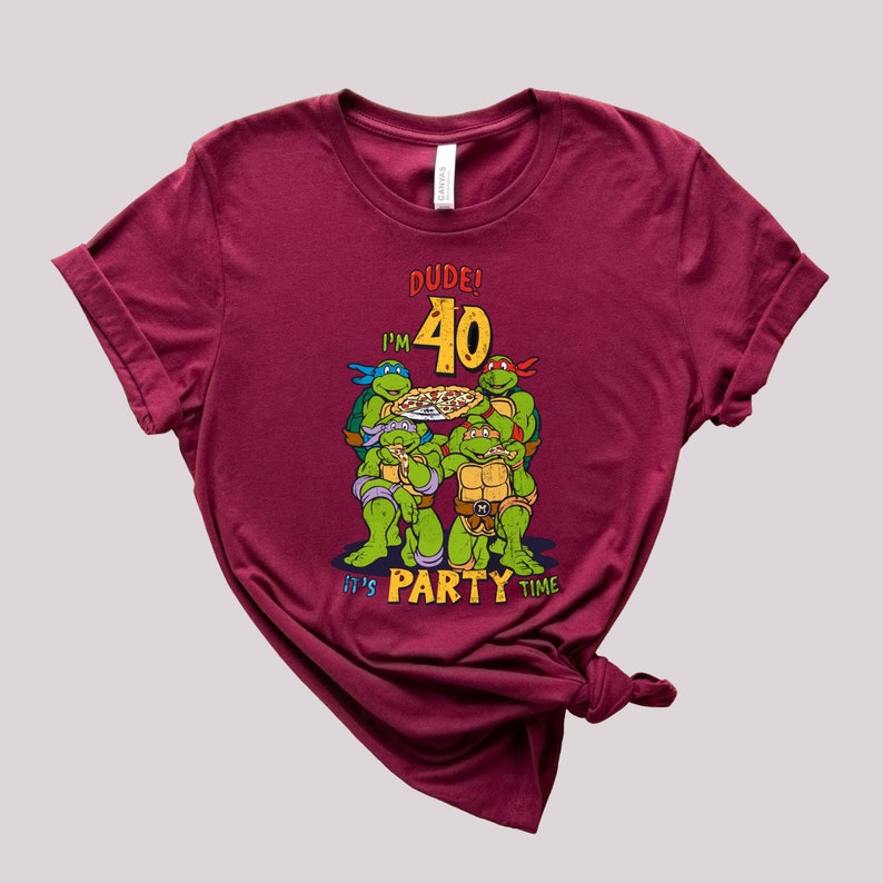 May include: A maroon t-shirt with a graphic of four Teenage Mutant Ninja Turtles holding pizza slices. The text "DUDE! I'M 40 IT'S PARTY TIME" is printed on the shirt.