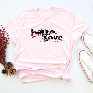 May include: Pink t-shirt with a black graphic that says "hello love" with red splatters.