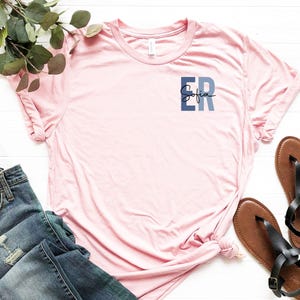 May include: A pink t-shirt with a blue and gray pocket design that says "Sofia ER" on it.