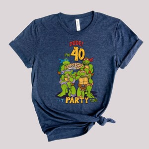 May include: A navy blue t-shirt with a graphic of four Teenage Mutant Ninja Turtles eating pizza. The text "Dude! I'm 40 It's Party Time" is printed on the shirt.