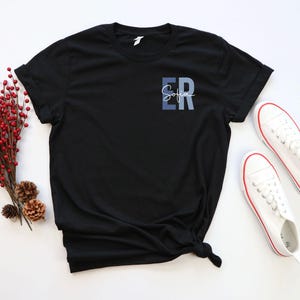 May include: Black t-shirt with a blue and white ombre design that says "ER Sofia" on the front.
