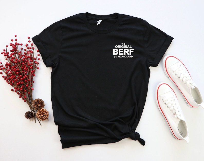 May include: Black t-shirt with white text that reads "The Original Berf of Chicagoland". The shirt is laid flat on a white surface with a pair of white sneakers beside it.