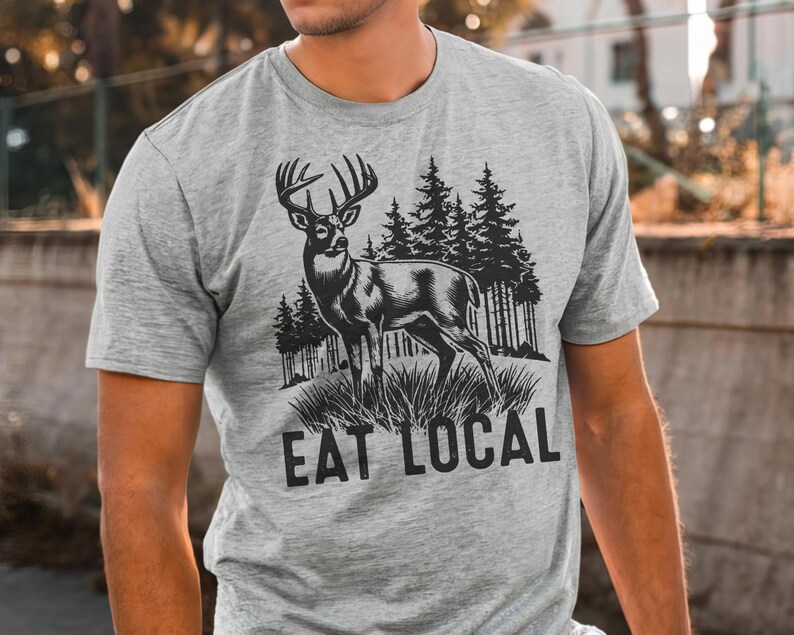 May include: A gray t-shirt with a black and white illustration of a deer in a forest setting. The text "Eat Local" is printed below the image.