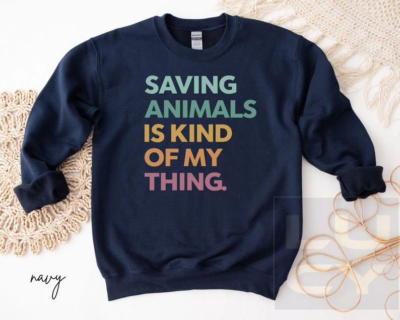 May include: Navy blue sweatshirt with the text "SAVING ANIMALS IS KIND OF MY THING" in teal, green, gold, orange, and pink. The sweatshirt has a crew neck and long sleeves. The word "navy" is written in cursive at the bottom left.