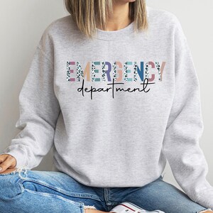 May include: A gray sweatshirt with the text "EMERGENCY department" in colorful letters with a white and black leopard print pattern.