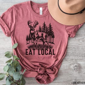 May include: Heather mauve t-shirt with a black silhouette of a deer and the text "Eat Local".