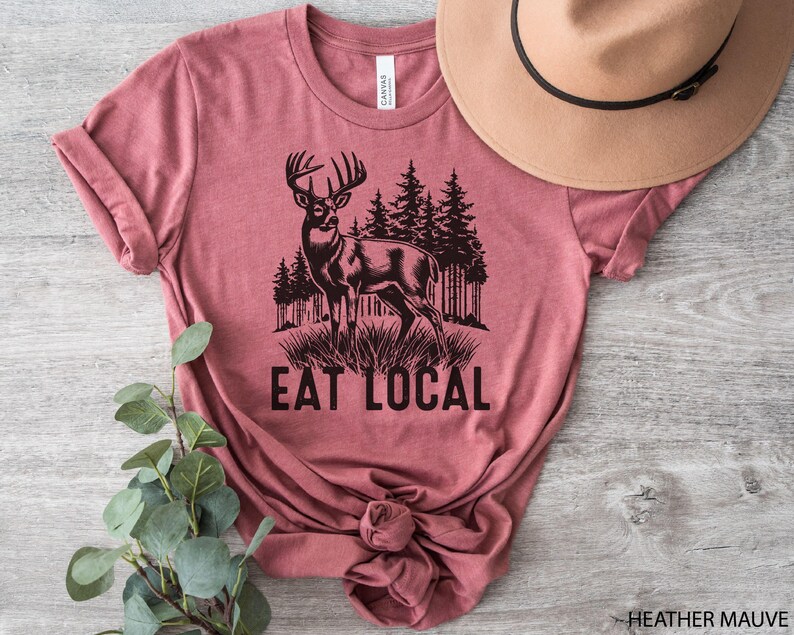 May include: Heather mauve t-shirt with a black silhouette of a deer and the text "Eat Local".