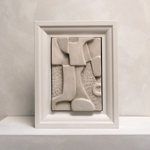 Puede incluir: Una escultura enmarcada en blanco con un diseño abstracto. La escultura está hecha de un material texturizado y tiene un diseño en relieve tridimensional.
