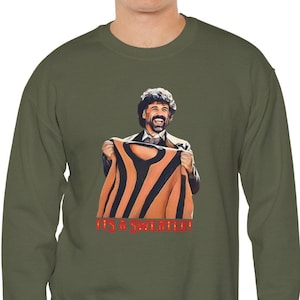 May include: A green long-sleeved sweatshirt with a graphic print of a man holding up a striped shirt and the text "It's a Sweater!"
