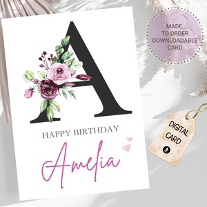 Op de afbeelding: Een witte verjaardagskaart met een grote zwarte letter "A" versierd met aquarel rozen en groen. De kaart leest "Happy Birthday Amelia" in een handgeschreven lettertype. Een label leest "Digitale kaart".