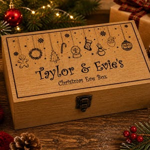 May include: A wooden Christmas Eve box with a decorative border and a metal clasp. The box is engraved with the names "Taylor & Evie's" and "Christmas Eve Box" along with Christmas-themed illustrations. The box is surrounded by Christmas decorations.