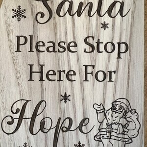 May include: Wooden sign with the words "Santa Please Stop Here For Hope" in a decorative font. The sign has a light wood grain background with engraved snowflakes and a Santa Claus illustration.