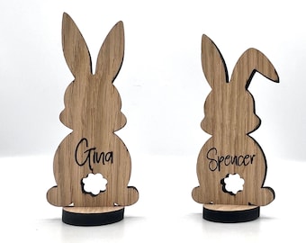 Op de afbeelding: Twee houten konijnen-kaartjeshouders met de namen Gina en Spencer erop gegraveerd. De konijnen staan op zwarte voetstukken.