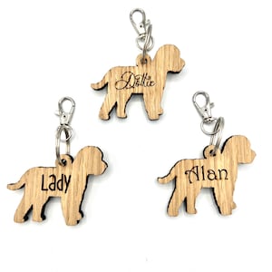 May include: Three wooden dog-shaped keyrings with silver clasps. Each keyring has a name engraved on it: "Dottie", "Lady", and "Alan". The keyrings are made of light-coloured wood.