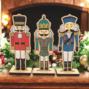 May include: Three wooden nutcracker figurines in red, green, and blue uniforms. Each has a unique design, including hats, mustaches, and decorative details. They stand on individual wooden bases, perfect for holiday decor.