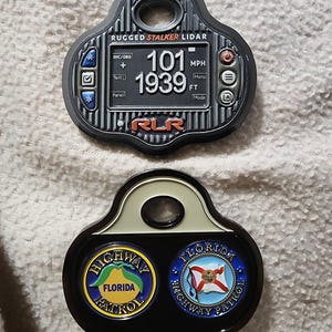 May include: Two black and gray metal keychains. The top keychain reads "RUGGED STALKER LIDAR" with a digital display showing "101 MPH" and "1939". The bottom keychain features two circular emblems with "FLORIDA HIGHWAY PATROL" text and logos.