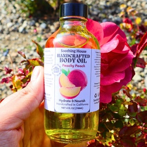 May include: A glass bottle of Peachy Peach body oil, handcrafted in California. The bottle is labeled with a peach illustration and the text "Soothing House Handcrafted Body Oil Peachy Peach Hydrate & Nourish Handcrafted in California NET 4 FL OZ (118ML)".