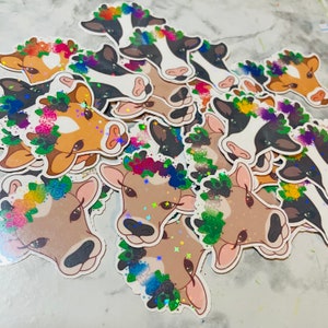 May include: A collection of cow stickers with rainbow flower crowns. The stickers are glossy and have a holographic glitter finish.