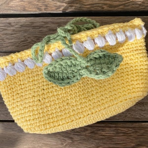 K&ouml;nnte beinhalten: Eine gelbe H&auml;keltasche mit wei&szlig;en und gr&uuml;nen H&auml;keldetails. Die Tasche hat ein Blattdesign und einen wei&szlig;en H&auml;kelrand.