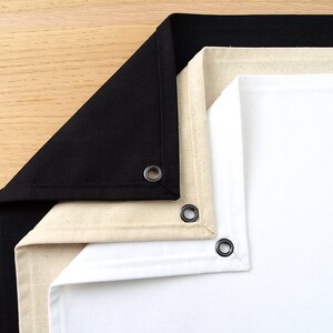 May include: Three fabric backdrops, one black, one beige, and one white, are folded together. Each backdrop has a metal grommet in the corner.