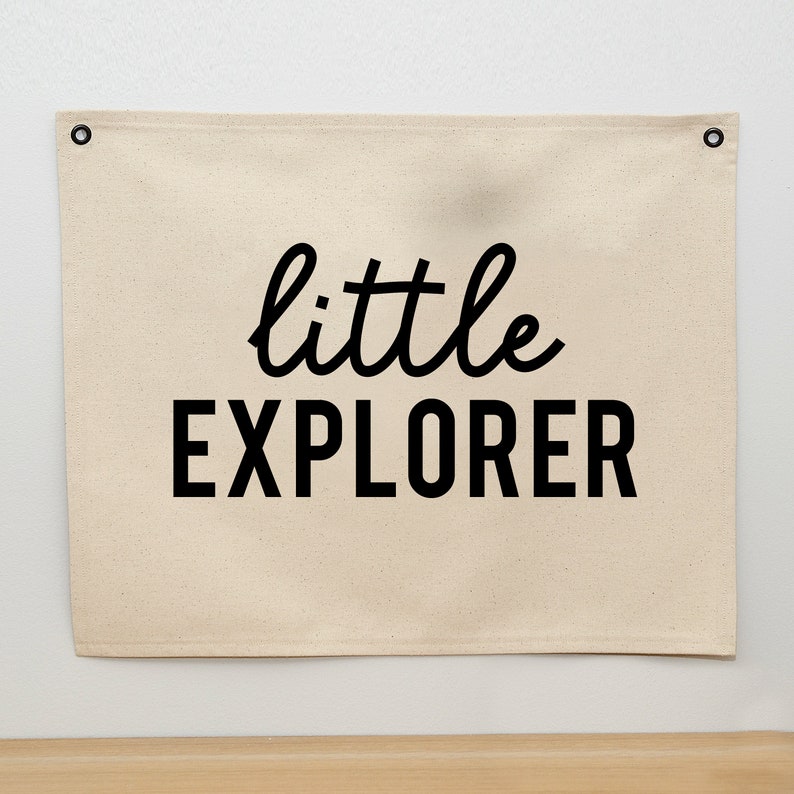 May include: A beige canvas banner with black grommets at the top corners. The banner has the text "little EXPLORER" printed in black.