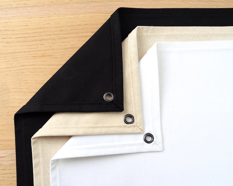 May include: Three fabric backdrops, one black, one beige, and one white, are folded together. Each backdrop has a metal grommet in the corner.