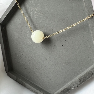Pu&ograve; includere: Una collana con catena dorata con un unico grande ciondolo rotondo bianco.