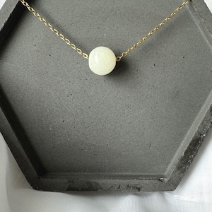 Pu&ograve; includere: Una collana con catena dorata e una singola perla bianca.