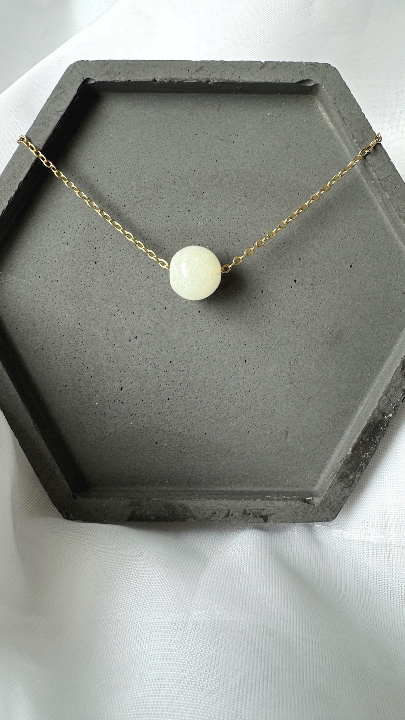 Pu&ograve; includere: Una collana con catena dorata e una singola perla bianca.