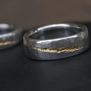 Puede incluir: Dos alianzas de plata con textura martillada. Una alianza tiene una fina l&iacute;nea dorada que recorre el centro.